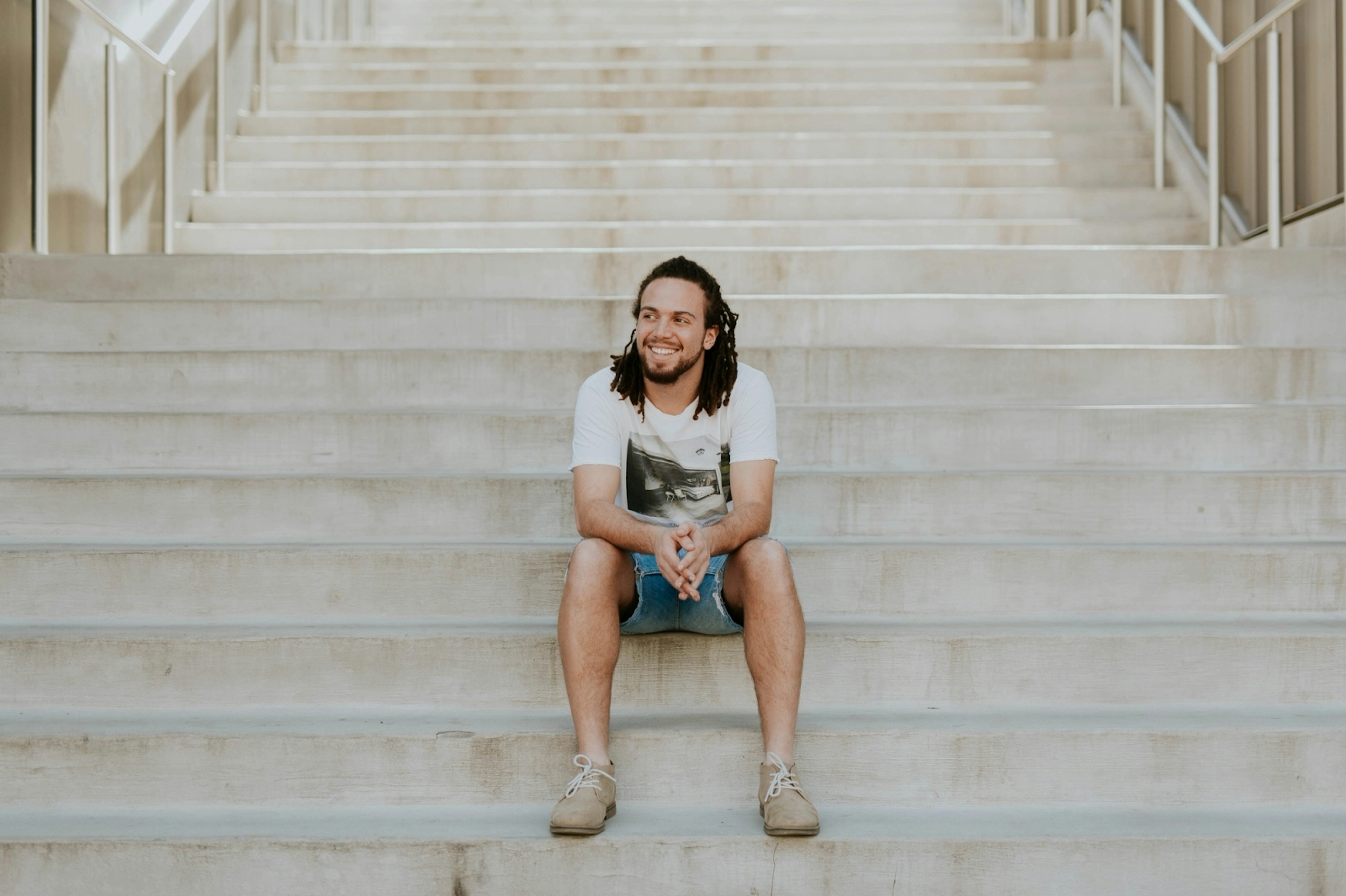 A smiling man with dreadlocks sits on a staircase
